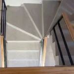 Vista desde arriba de escalera con baranda de hierro negro, pasamanos de madera y pared de tablillas, Temperley